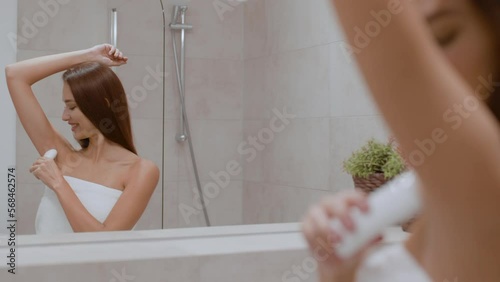 Everyday hygiene. Young positive lady wrapped in towel applying antiperspirant on her armpit in morning, free space