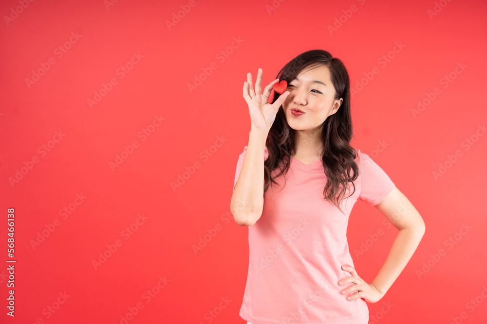 Beautiful Asian woman with pink shirt holding small little heart isolated over red background. Valentines Day concept. Feel joy and romance Beautiful Asian woman with pink shirt holding small little heart isolated over red background. Valentines Day concept. Feel joy and romance