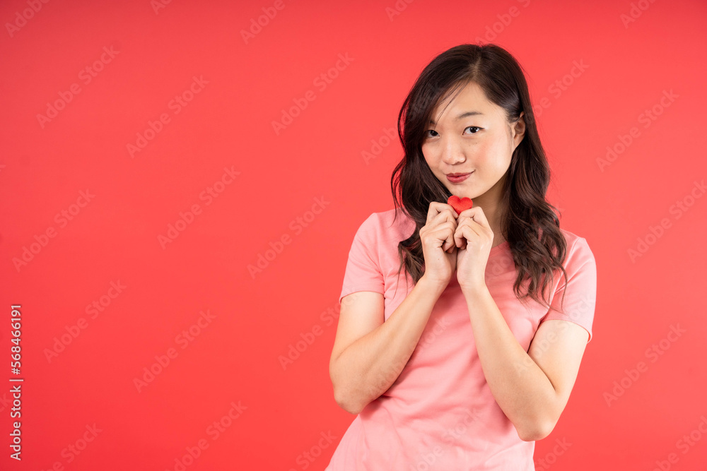 Fototapeta premium Young Asian woman with pink shirt feel romance holding small little heart isolated over red background. Valentines Day concept.