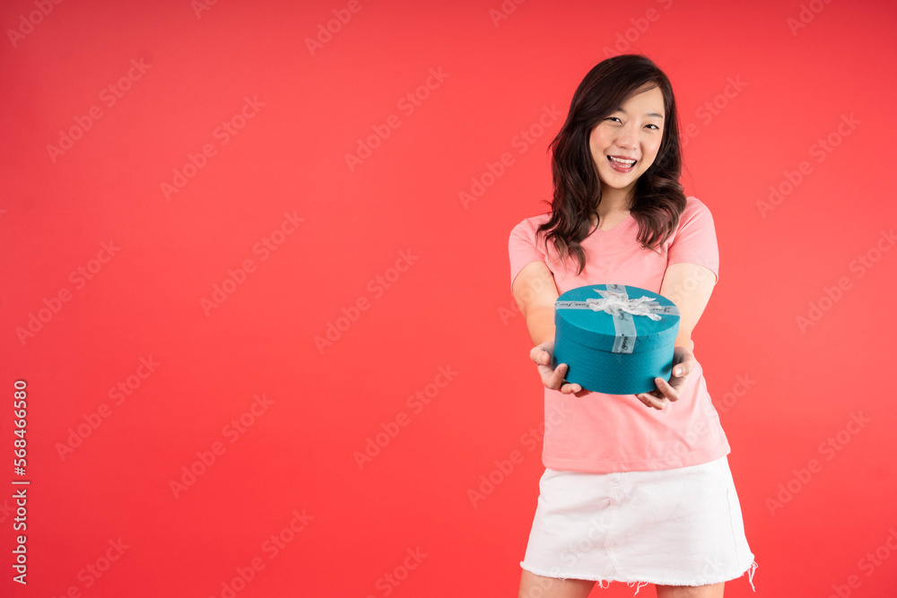 Happy beautiful Asian woman smile with blue gift box isolated on red background. Teenage girls in love, Receiving gifts from lovers. New Year, Christmas and Valentines Day concept Happy beautiful Asian woman smile with blue gift box isolated on red background. Teenage girls in love, Receiving gifts from lovers. New Year, Christmas and Valentines Day concept