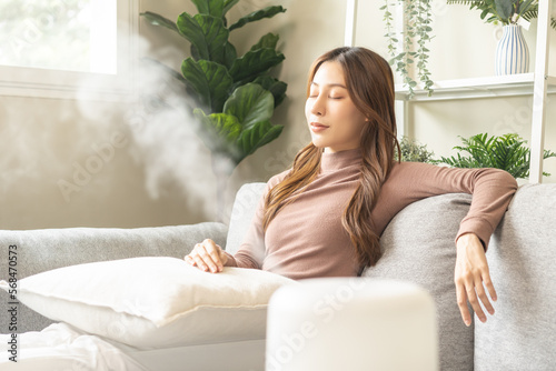 Modern air humidifier during relax or rest, happy asian young woman, girl enjoying aromatherapy steam scent from essential oil diffuser comfortable in living conditions room, apartment at home. photo