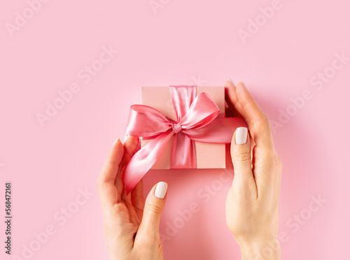 Womans hands holding wrappes gift box with ribbon on pink background © Denira