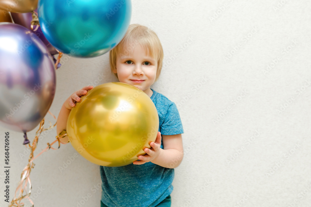 Blond cute happy Child kid boy celebrating third birthday with colorful balloons at party,home in front of wall.baby smiling looking at camera.adorable caucasian baby.Festive background decoration Blond cute happy Child kid boy celebrating third birthday with colorful balloons at party,home in front of wall.baby smiling looking at camera.adorable caucasian baby.Festive background decoration