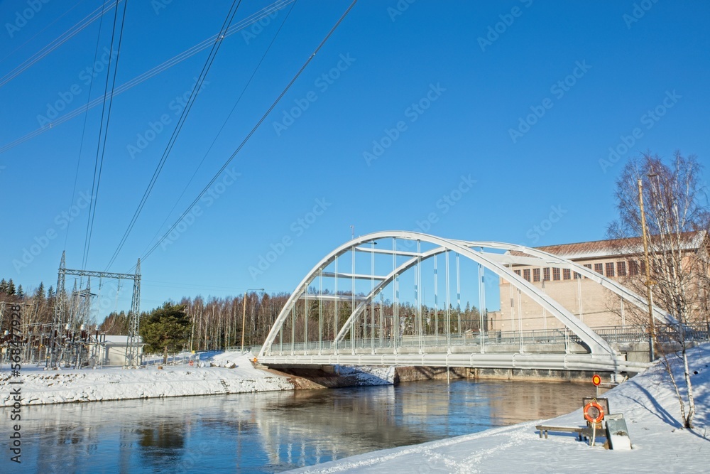 Fototapeta premium Modern bridge with snow on the ground and river flowing without ice in winter at Ahvenkoski, Pyhtää, Finland.