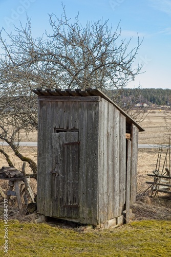 Old wooden outhouse in countryside in sunny spring weather.