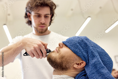 Barber shaving bearded man in barber shop.