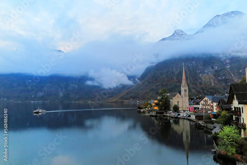 Morning scenery of Hallstatt, a lakeside village in Salzkammergut area of Austria, with a boat cruising on the lake, mountains houses reflected in the water colorful autumn forests the on hillside