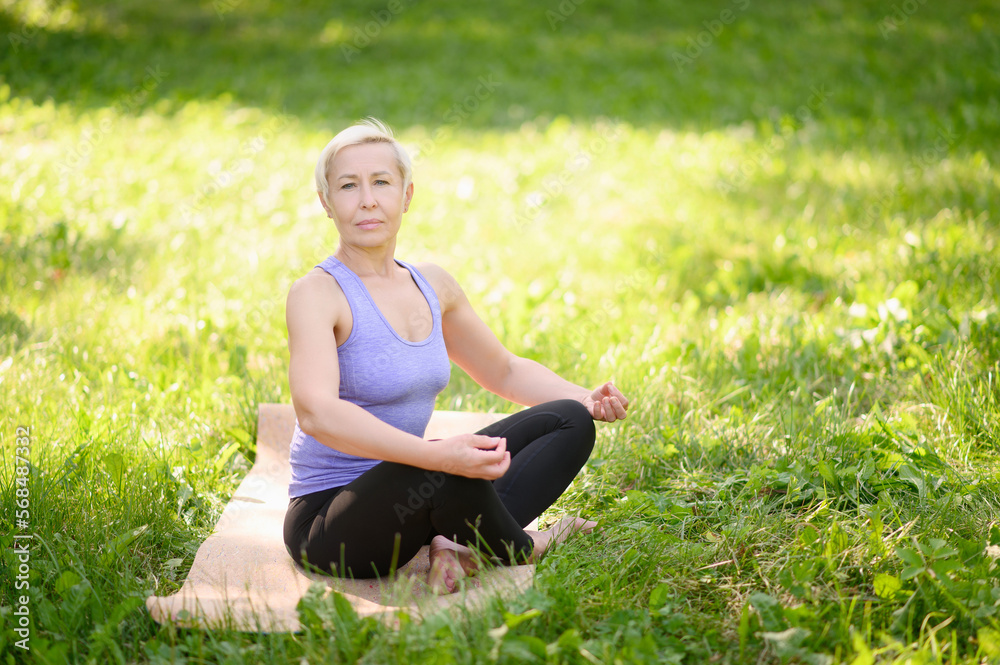 Happy athletic middle aged woman doing yoga outdoors barefoot in lotus position.Does sports in the city park. The concept of meditation. Happy athletic middle aged woman doing yoga outdoors barefoot in lotus position.Does sports in the city park. The concept of meditation.