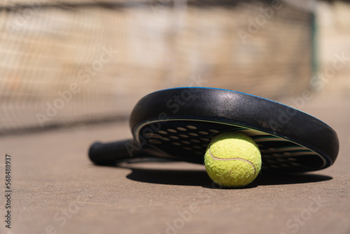 From below of yellow padel ball placed under black racket near net on sunny day © diignat