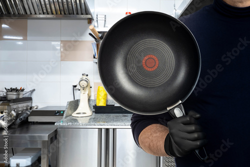 Non-stick frying pan in mans hand. Cropped chef shows off quality frying pan. Inventory for kitchen of restaurant concept. Frying pan with removable handle for cooking hot dishes. photo