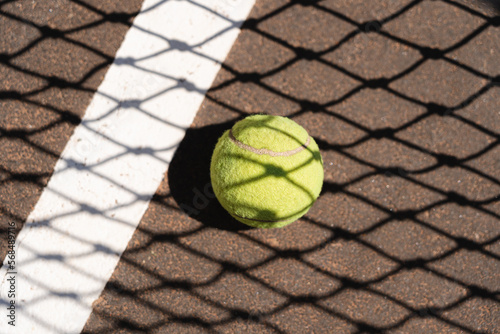 Top view of yellow tennis ball placed on court and covered with shadow of net on sunny day © diignat