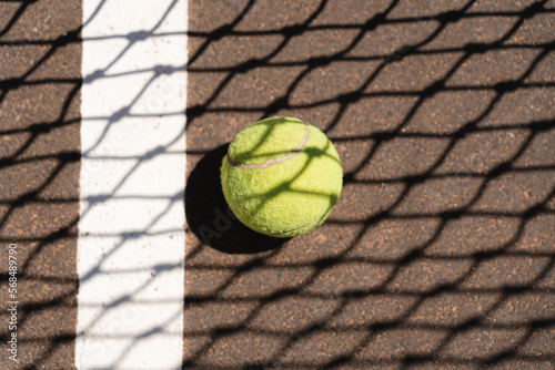 Top view of yellow tennis ball placed on court and covered with shadow of net on sunny day