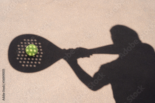 High angle of yellow ball placed on court and covered with shadow of crop person holding padel racket