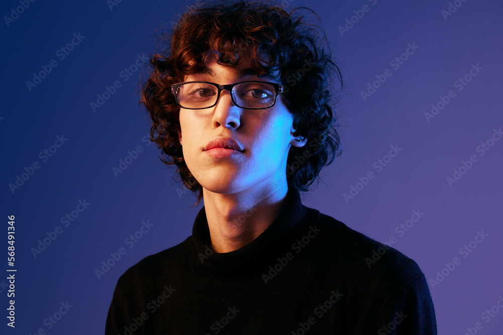 Man fashion portrait in black clothes model poses in close-up glasses, curly hair, hipster lifestyle, portrait blue background, mixed neon light, fashion style and trends boys teenager, copy space