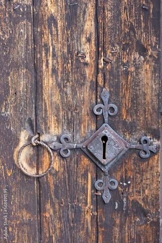 Keyhole of old metal lock on a weathered wooden door with a metal ring door handle.