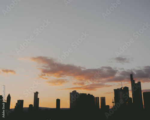 Captivating view of Frankfurt's iconic skyline as the sun sets, casting an orange hue over the city and surrounding clouds