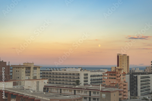 Take in the magnificent sunset with the moon shining over the city's vibrant rooftops