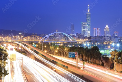 Night scenery of Taipei City with view of Taipei 101 Tower in downtown, MacArthur Bridge across river and car trails on Dike Avenue ~ Taipei cityscape at dusk by riverside (long exposure effect)
