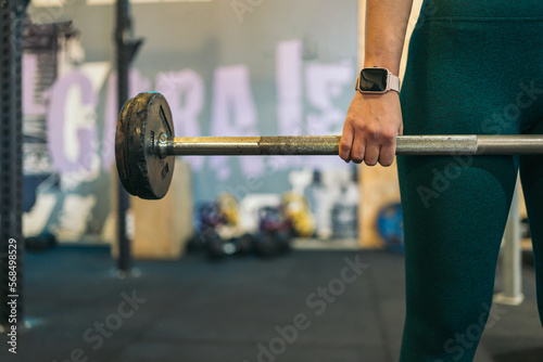 Cropped image of a young sporty woman in the gym holding a barbell.