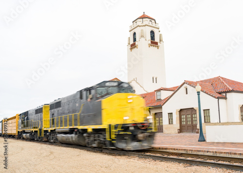 Train speeds past a depot with tall clock tower photo