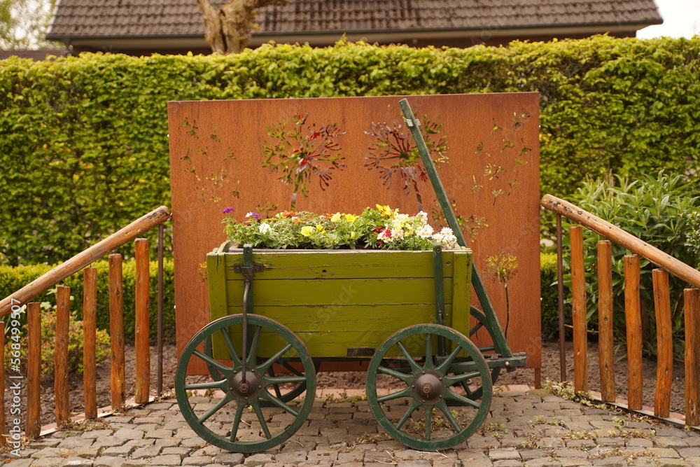 An old wooden cart overflowing with pink petunias and other colorful flowers