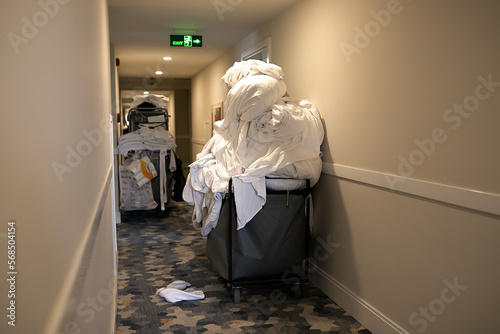 Cleaners trolley with cleaning equipments at hotel. Trolley full of dirty white sheets of guests in a hotel.