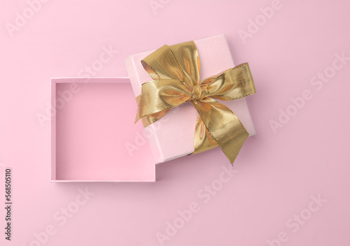 Pink empty gift box open with golden golden bow and ribbon