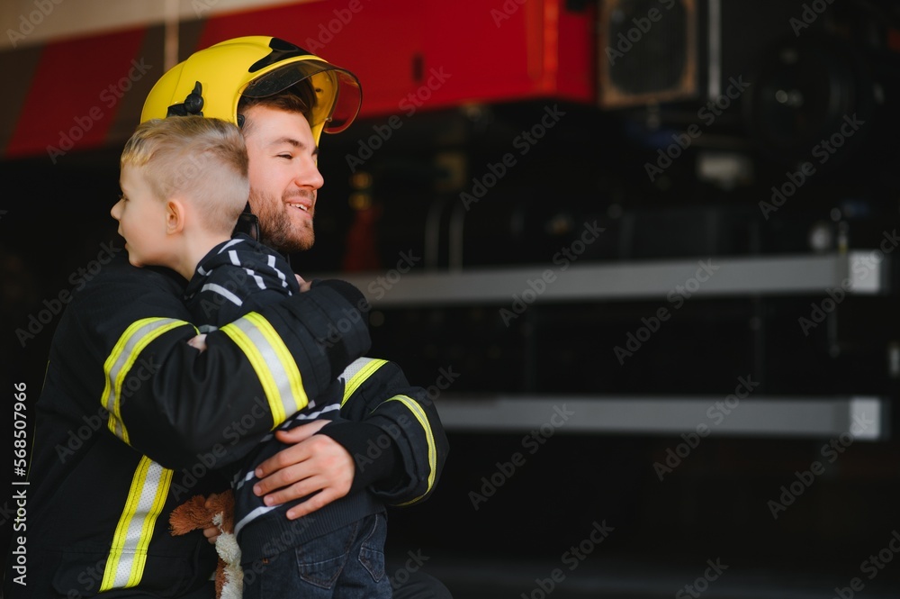 Fototapeta premium Dirty firefighter in uniform holding little saved boy standing on black background.