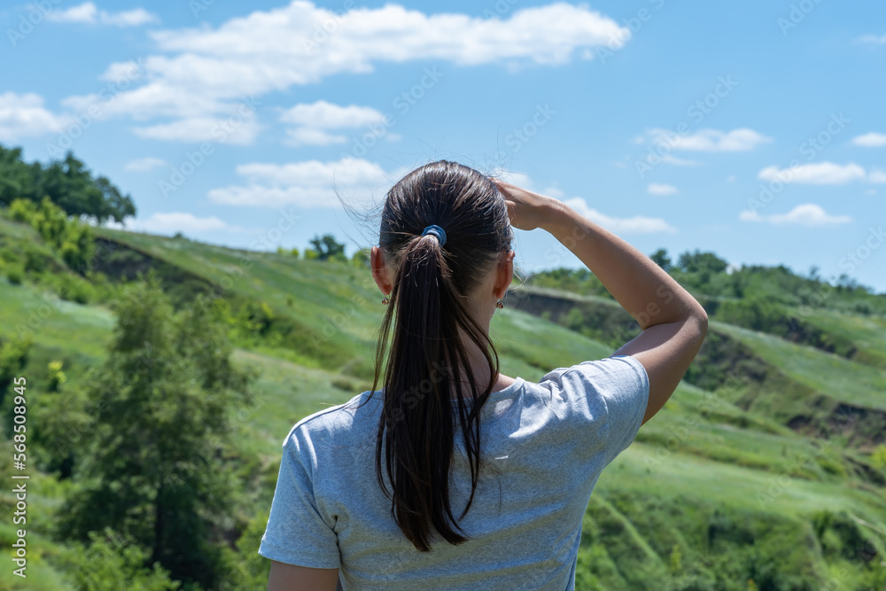 Woman looking on ravine covered with greenery. Young female traveler see landscape valley with geological faults. She admires earthen mountains and relief. Girl explore world. Positive emotion.