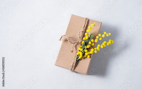 Gift craft box with yellow mimosa flowers on a light background. The concept for the spring holiday of women's Day or mother's day.