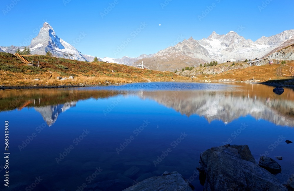 Morning scenery of Mountain Matterhorn towering under blue sunny sky with reflection in the peaceful, clear water of Lake Leisee in Sunnegga, Zermatt, canton of Valais, Switzerland, Europe