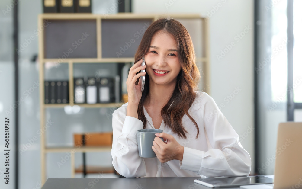 Smiling Asian businesswoman enjoying a phone call with a client in the office. Smiling Asian businesswoman enjoying a phone call with a client in the office.