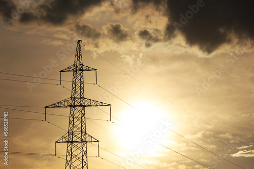 Silhouette of high voltage tower with electrical wires on background of sunset sky and dark clouds. Electricity transmission lines, power supply, blackout concept