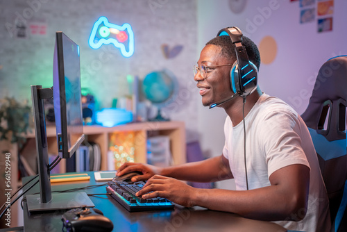 Streamer young man professional gamer play online games computer with headphones, colorful neon room
