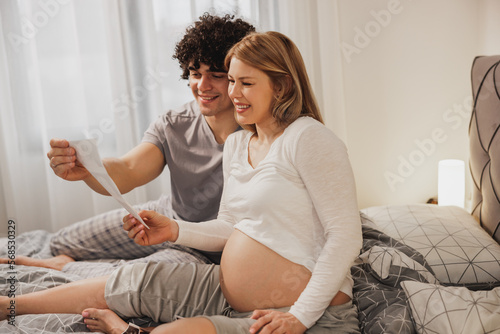 Pregnant Couple Looking At Ultrasound On A Bed