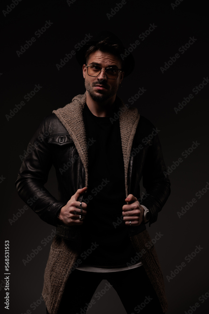 sexy bearded guy with glasses pulling and adjusting leather jacket