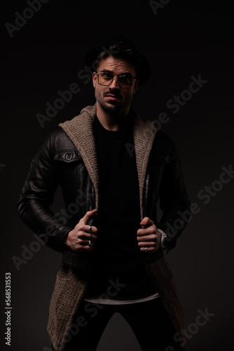 sexy bearded guy with glasses pulling and adjusting leather jacket