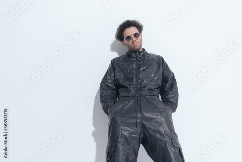 greek fashion model with curly hair in leather suit holding hands in pockets