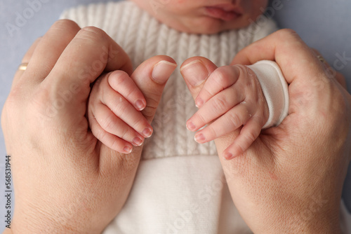 The newborn baby has a firm grip on the parent's finger after birth. Close-up little hand of child and palm of mother and father. Parenting, childcare and healthcare concept. Professional macro photo.