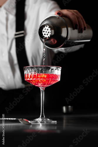 the bartender makes a kir royal cocktail in a  crystal glass on a dark background