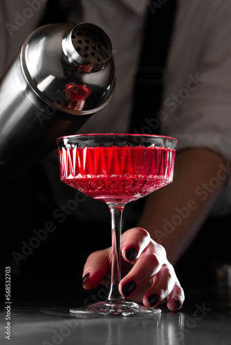 the bartender makes a kir royal cocktail in a  crystal glass on a dark background