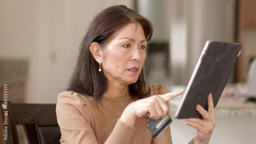 Attractive woman relaxing shopping online with mobile tablet and e-commerce credit card excited with buying sitting in peaceful leisure home successful at buying. Mature asian is successful.. Attractive woman relaxing shopping online with mobile tablet and e-commerce credit card excited with buying sitting in peaceful leisure home successful at buying. Mature asian is successful..