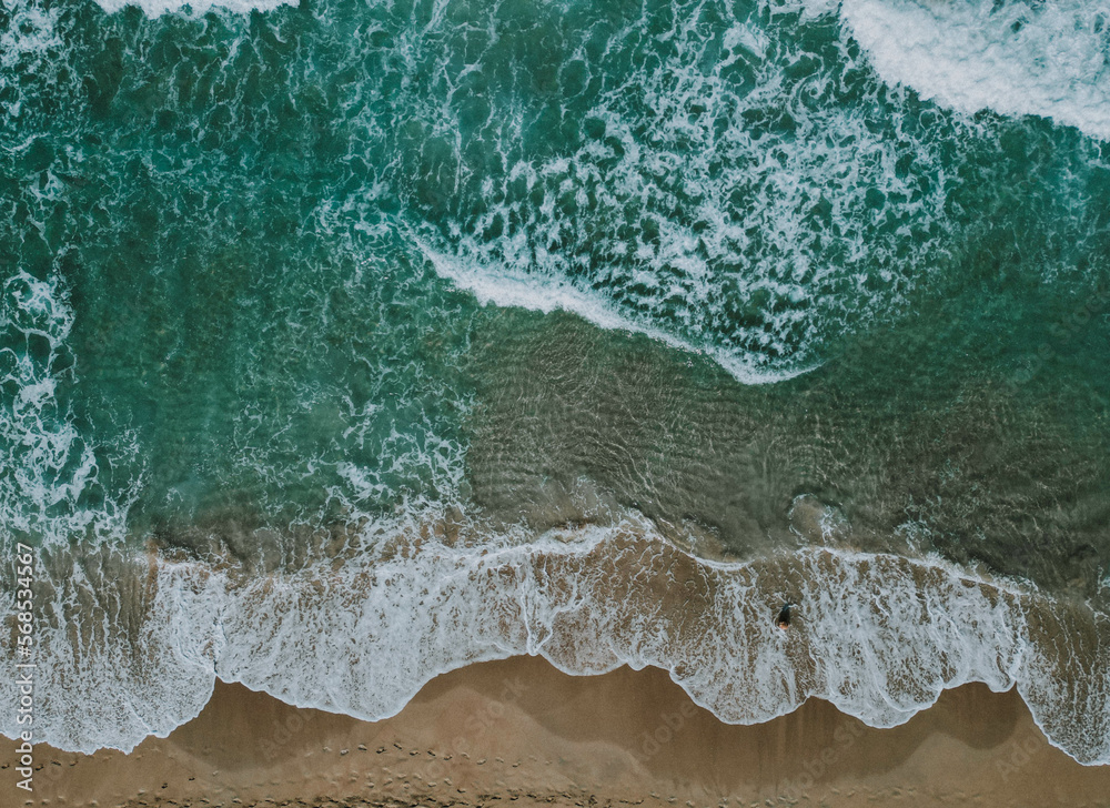 Drone aerial view: Turquoise water, white waves, and sandy beach from above