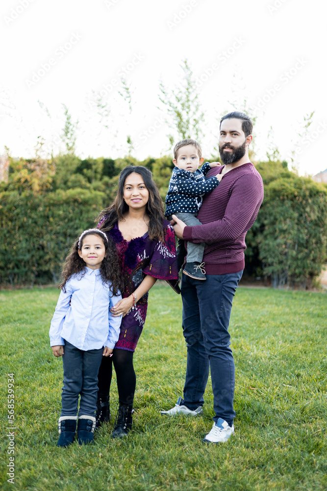 The interracial family is active and enjoys a day at the park. Successful adoption. The family poses standing as they look into the camera. Concept of multiethnic or interracial family. The interracial family is active and enjoys a day at the park. Successful adoption. The family poses standing as they look into the camera. Concept of multiethnic or interracial family.