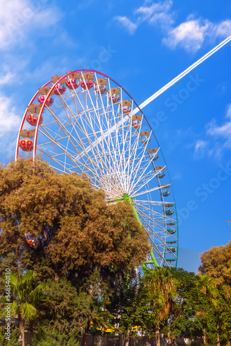 Ferris wheel on the background of an airplane flying through the blue sky. Ayia Napa. Cyprus. photo
