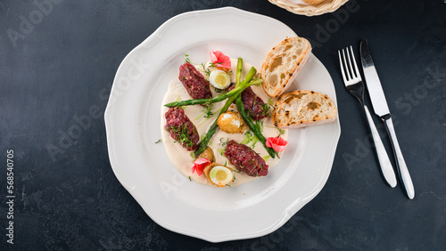 Beef tartare with with asparagus, herbs, sauce and slices of bread.