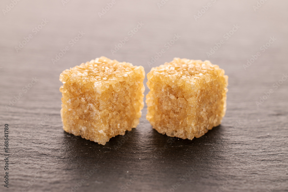 Two brown sugar cubes, close-up, on a slate board.