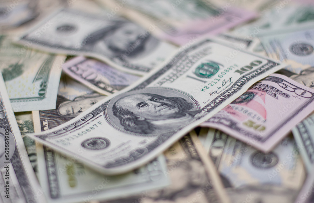 One hundred dollars close-up in large quantities lie on the table. Scattered money lies in the background all over the surface. Blurred background on a hundred dollar bill. One hundred dollars close-up in large quantities lie on the table. Scattered money lies in the background all over the surface. Blurred background on a hundred dollar bill.