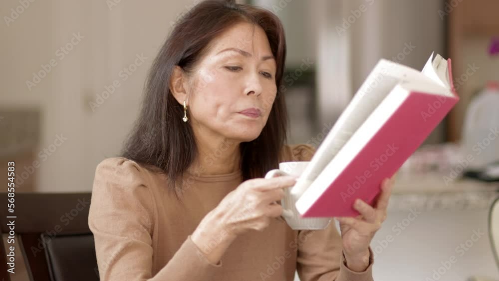 Attractive woman relaxing reading book drinking coffee sitting in comfortable leisure home. Mature asian has healthy lifestyle. Attractive woman relaxing reading book drinking coffee sitting in comfortable leisure home. Mature asian has healthy lifestyle.