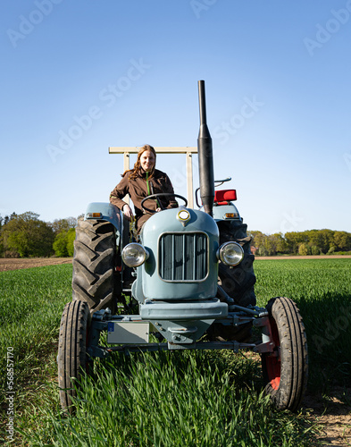 Junge Frau mit Spass an der Landwirtschaft sitzt auf einem Oldtimer - Traktor mitten im Getreidefeld bei Sonnenschein. photo